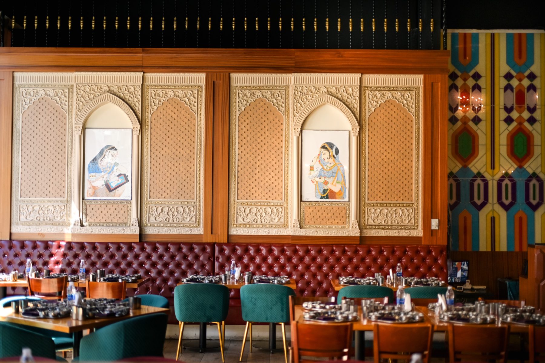 The carved plaster wall, with Rajasthani miniatures set into its arched niches above the banquettes