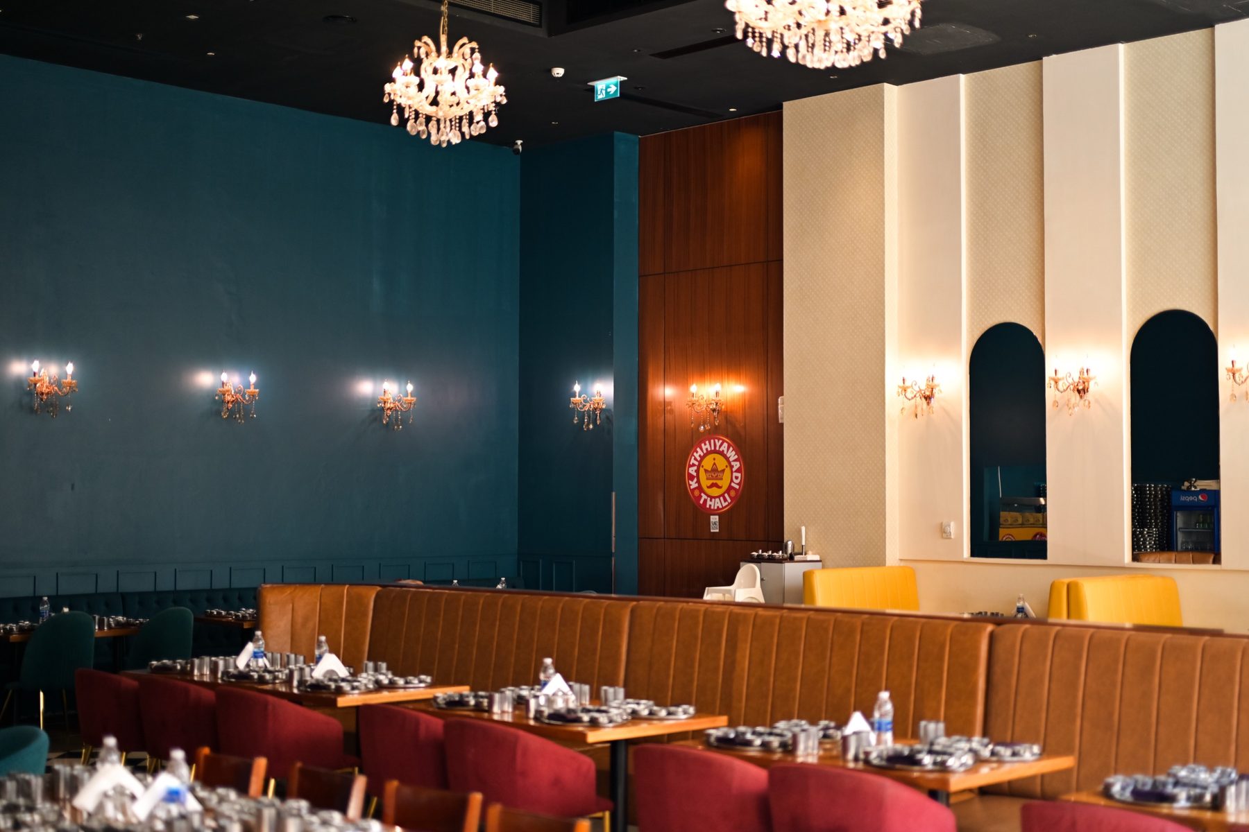 The dining room, with petrol-teal walls, brass wall lights and long tables already laid with steel thalis