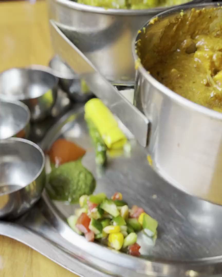A pot of dal held over a thali, mid-service, with salad and chutneys already in the tray